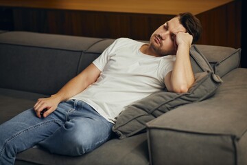 A young man in a white T-shirt, exhausted, fell asleep in front of the TV.