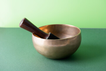 Tibetan singing bowl with sticks used during mantra meditations on green background, close up. Sound healing music instruments for meditation, relaxation, yoga, massage, mental health