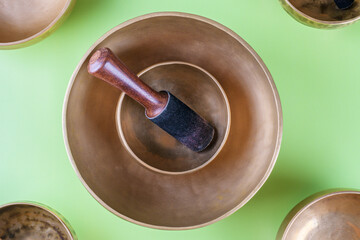 Tibetan singing bowls with stick used during mantra meditations on green background, top view, flat lay. Sound healing music instruments for meditation, relaxation, yoga, massage, mental health
