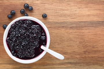 Fresh homemade jam made of Patagonian Calafate berries (lat. Berberis heterophylla) served in white bowl, photographed overhead on wood with copy space on the side (Selective Focus, Focus on the jam)