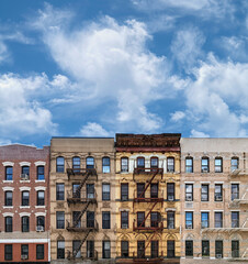 Block of New York City style old apartment buildings with empty blue sky and fluffy white cloud...