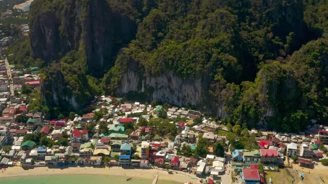 High aerial tilt down view of cityscape to reveal mountains and blue waters of Corong Beach in El Nido, Palawan, Philippines