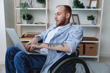 A man in a wheelchair freelancer works at a laptop at home, work online, social networks and...