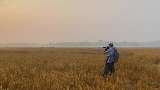 Wide shot of man wearing winter clothes taking pictures with camera of harvest field