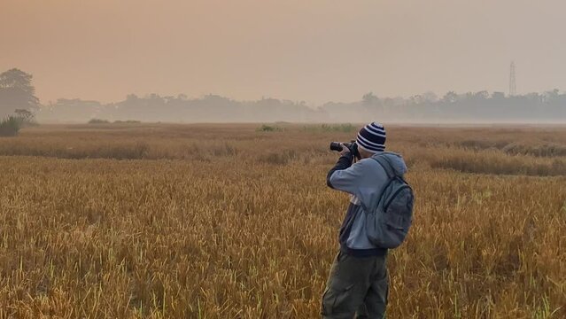 Profile wide view of photographer on field taking pictures of polluting industry