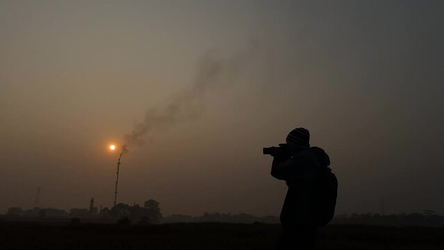 Silhouette of photographer with camera taking pictures on environment pollution. far away gas plant burning smoke