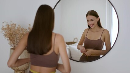 Slimming and dieting result. Young happy sporty woman checking her body condition, measuring her waist with tape