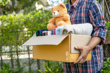 Holding clothing donation box with used clothes and doll at home to support help for poor people in...