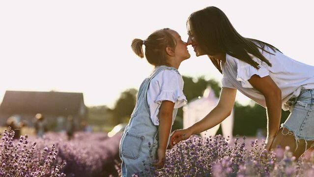family day. young mom and little daughter enjoy relaxing in a field with lavender at sunset. A beautiful mother hugs and kiss child girl tightly. Maternal care and love for the child. mothers day.