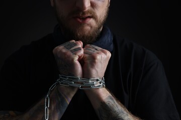 Man with chained hands on dark background, closeup. Hostage