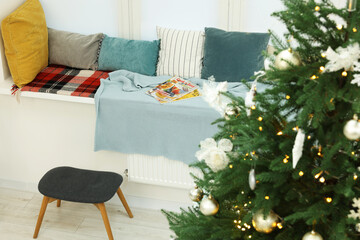 Beautiful Christmas tree near cozy window sill with pillows in room. Interior design