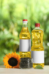 Bottles of sunflower cooking oil, seeds and yellow flower on white wooden table outdoors