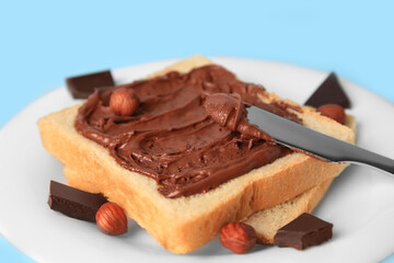 Spreading chocolate paste onto bread on light blue background, closeup