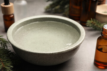 Obraz na płótnie Canvas Bowl of essential oil and fir twigs on grey table, closeup. Aromatherapy treatment