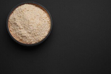 Bowl of brewer`s yeast flakes on black background, top view. Space for text
