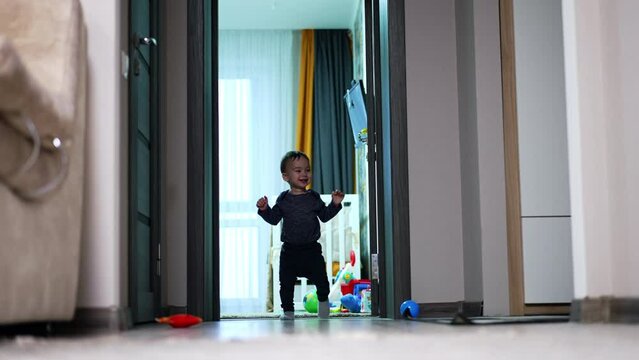 Active happy toddler rises on his feet and walks holding hands up. Smiling kid falls on the floor and starts to crawl quickly.