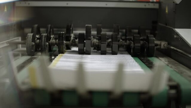 Close up of a printing machine, peper traveling on the production line and stopping on the curved end of the machine.