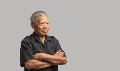 Portrait of an elderly Asian man in a shirt looking away with a smile while standing arms crossed on a gray background