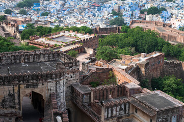 Top view of Mehrangarh fort with distant view of blue city Jodhpur, Rajasthan, India. Blue sky with white clouds in the background. One of the seven gates to enter the huge fort is seen below,
