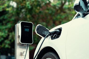 Focus closeup electric vehicle plugged in with EV charger device from blurred background of public...