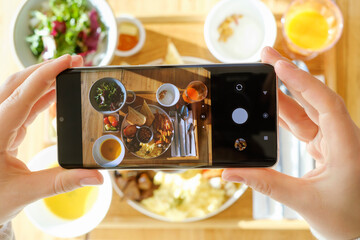 Female hands taking pictures of their breakfast on mobile phone, top view.