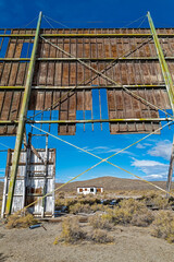 The concession stand and projector building is framed by the damaged wood screen at an abandoned drive-in movie theater