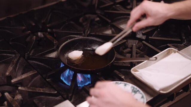man puts the chicken with a silver skewer in a frying pan with hot oil in a restaurant kitchen. Close up shot