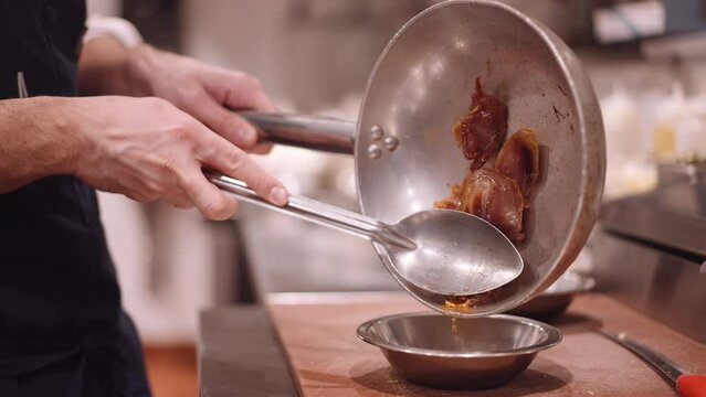 Male cook holds the meat in the frying pan with a silver spoon so the fat can drip from the tub. Close up dolley shot