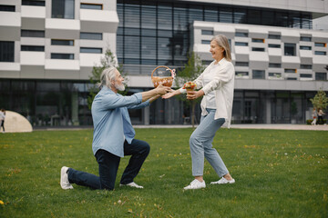Senior man standing on a grass in summer and give straw basket to woman