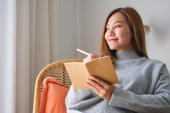 Portrait image of a young woman holding and writing on notebook at home