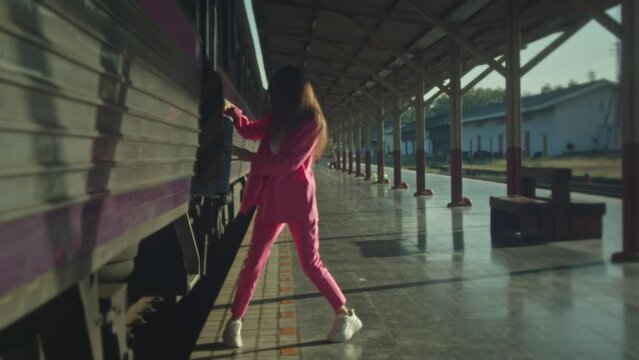 A young woman in a pink suit steps off the train onto the ground and walks away