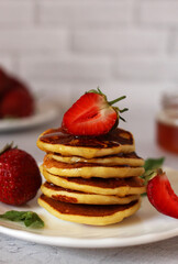 small pancakes stacked on a plate with strawberries and honey on a light background