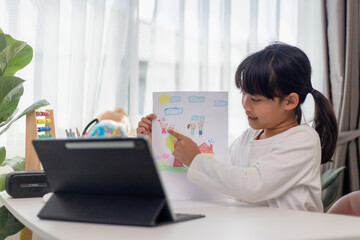 Asian schoolgirl doing her homework with digital tablet at home. Children use gadgets to study. Education and distance learning for kids. Homeschooling during quarantine. Stay at home