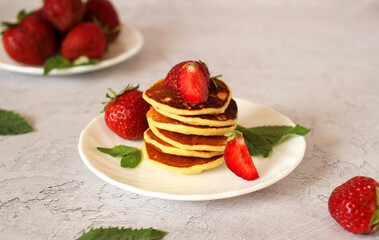 small pancakes stacked on a plate with strawberries on a light background