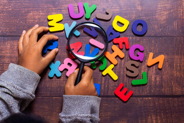The child holds a magnifying glass, looking for English letters. English alphabet made of square...