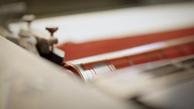 Printing roller turning on the machine covered in light red color, close up.