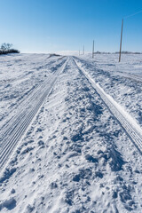 Fototapeta na wymiar Vehicle tracks through deep snow on a rural road in Saskatchewan, Canada