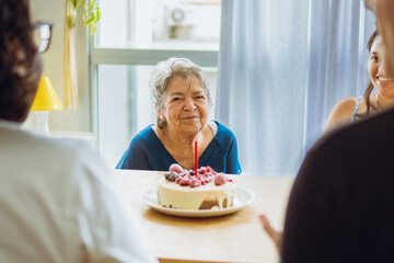 Elderly latin woman sitting in the dining room of her home in front of her birthday cake together...