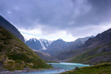 Mountain lake calm turquoise with clear water Karakabak in the Altai mountains with snow and glaciers under thick clouds.