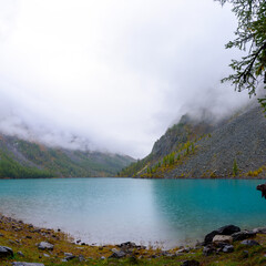 Rain on the alpine turquoise lake Shavlinskoe among the rocks with haze of fog and raindrops in Altai.