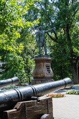 Fototapeta premium Monument to Peter I in Petrvsky Square. Bronze statue of king is mounted on pedestal made of pink Pavlovsk granite. Ship guns near monument. Fountain in background. Voronezh, Russia - July 30, 2022