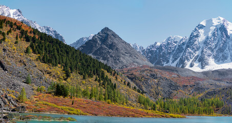 Panorama of Lake Shavlinskoye with a stone mountain similar to a pyramid against the background of rocks with tongues, glaciers and snow in Altai in the sun.