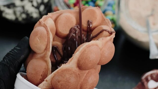 Pouring hot melted chocolate on a bubble waffle. Person making waffles.