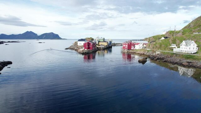 Old Norwegian traditional fishing village on a nice calm summer day, while a boat just left the harbor, Aerial Forwarding shot