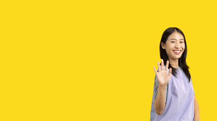 Waving hand in hi, Asian woman smiling friendly greeting, Hello,nice to meet you,say hi, Say hi and greet you, Welcome new people Join a multicultural team, Goodbye, Isolated on yellow background.