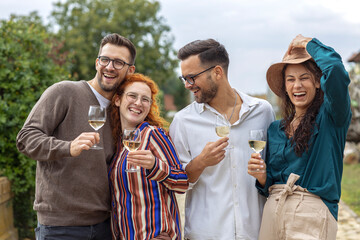 Four friends in vineyard talk to each other and smile with glass of vine in hands