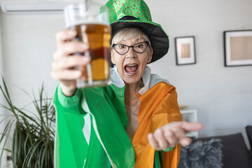 Mature woman with irish flag on shoulders holding glass of beer and celebrate saint patrick day