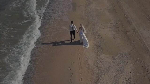 The bride and groom in wedding clothes are walking along the seashore, hugging, kissing, running, enjoying themselves. Husband and wife are filming a clip in a hotel on vacation. Lovely couple look at