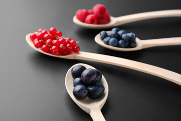 Wooden spoons with fresh berries on dark background, closeup