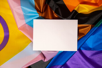 Empty paper blank on Rainbow LGBTQIA flag made from silk material. Mock up template copy space for your text. Symbol of LGBTQ pride month. Equal rights. Peace and freedom. Support LGBTQIA community